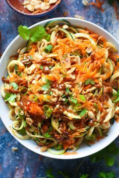 a white bowl filled with noodles and sauce on top of a blue tablecloth next to two bowls of food