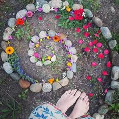 the person is standing in front of a circle made out of rocks and flowers on the ground