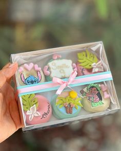 a hand holding a clear box with decorated cookies in the shape of animals and palm trees