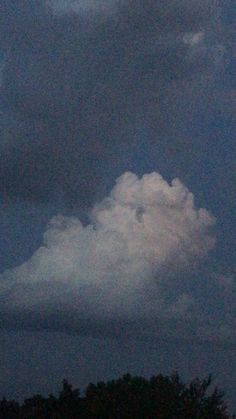 an airplane flying in the sky with clouds above it and trees behind it, at night