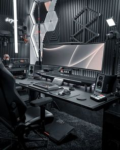 a computer desk with two monitors and speakers on it in front of a black wall