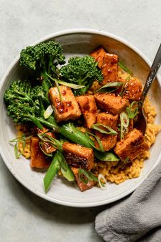 a white bowl filled with tofu and broccoli on top of yellow rice