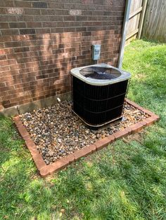 an air conditioner sitting in the grass next to a brick wall