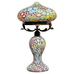 a multicolored glass lamp sitting on top of a metal stand next to a white wall