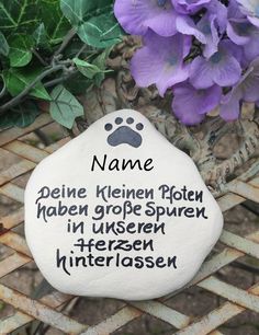 a pet memorial stone with a dog's paw and name on it next to purple flowers