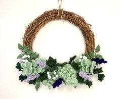 a crocheted wreath with green leaves and purple flowers