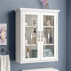 a white cabinet with glass doors in a blue walled room next to a towel rack