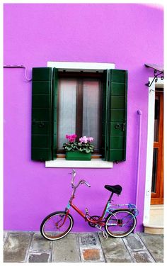 a bike parked in front of a purple building with green shutters and flowers on the window sill