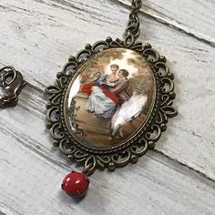 Here is a handmade necklace that was made using a rare mustard and red acrylic lovers cameo. The cameo is made in a fun French baroque style. It is made form an acrylic. It is set in a scalloped edge setting with a vintage red rhinestone dangle. The pendant hangs on an antique brass chain that closes with a lobster claw clasp.Size Pendant 2 7/8 by 1 7/8 inches Chain 25 inches Vintage Bronze Necklaces For Valentine's Day, Vintage Bronze Necklace For Valentine's Day, Red Cameo Jewelry Gift, Red Vintage Necklace With Charm, Vintage Red Round Pendant Necklace, Red Cameo Necklace For Gift, Red Vintage Oval Pendant Necklace, Red Oval Pendant Vintage Necklace, Handmade Victorian Red Necklace