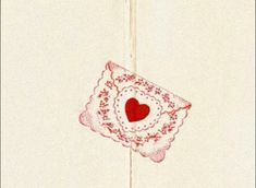 a red heart is hanging on the side of a white wall with an embroidered doily