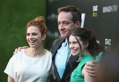 two women and a man standing next to each other in front of a red carpet