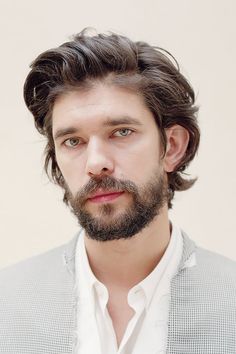 a man with long hair and a beard wearing a gray jacket looking at the camera