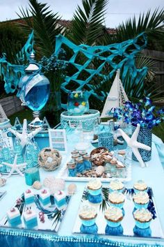 a blue table topped with cupcakes and desserts next to palm trees in the background