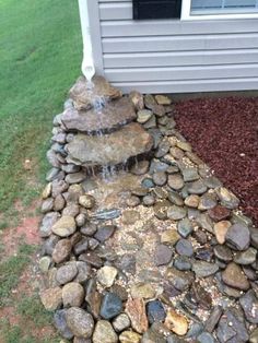 a rock waterfall in front of a house with grass and rocks on the ground next to it