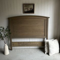 a bedroom with white walls and wooden headboard next to a potted plant on the floor