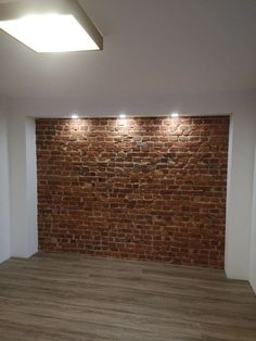 an empty room with brick wall and wood flooring in the corner, lighting up