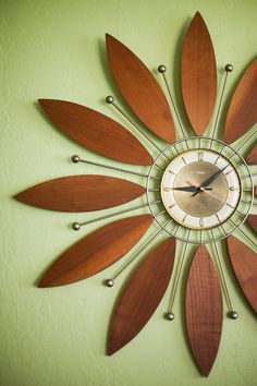 a clock that is mounted to the side of a wall with wooden leaves on it