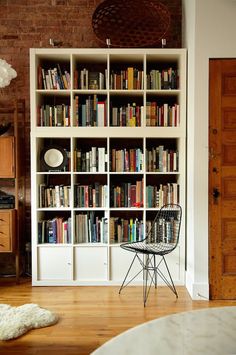 a book shelf filled with lots of books next to a white chair and wooden table