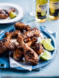 grilled chicken on a blue plate with lime wedges and two bottles of beer