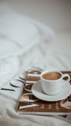 a cup of coffee sitting on top of a white saucer next to a magazine