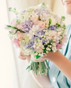 a woman holding a bouquet of purple and white flowers in front of a window with curtains