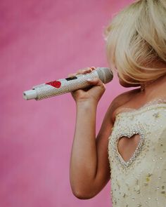 a blonde woman in a white dress holding a microphone to her ear and looking into the distance