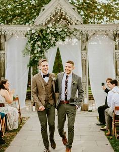 two men are walking down the aisle at an outdoor wedding ceremony, one is wearing a suit and the other has a tie