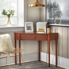 a wooden desk with a gold lamp and pictures on it next to a chair in front of a window