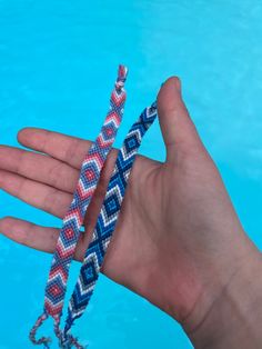 a hand holding two bracelets in front of a swimming pool with blue and red water