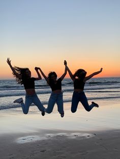 three women jumping in the air on a beach at sunset with their arms up and legs spread out