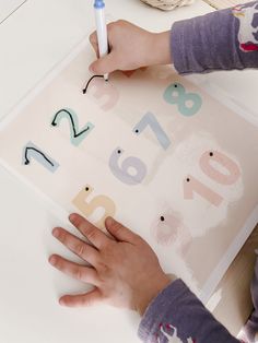 a child's hands writing on a piece of paper with letters and numbers in the background