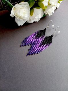 a pair of purple and black beaded earrings next to white flowers