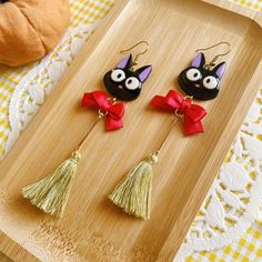 two black cats with red bows and tassels are on a wooden tray next to a pumpkin