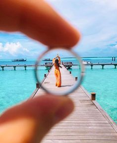 a person holding a magnifying glass looking at the water and pier with boats in the background