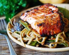 a close up of a plate of food with noodles and salmon on it, next to broccoli