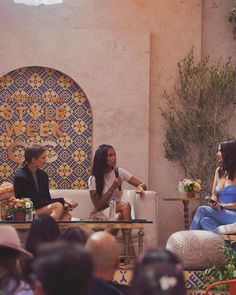 three women sitting on chairs talking to each other in front of a group of people