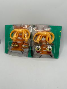 two plastic toys in the packaging on a white surface with green trim and yellow handles