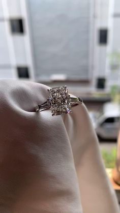 a cushion cut diamond engagement ring sitting on top of a white satin pillow in front of a window