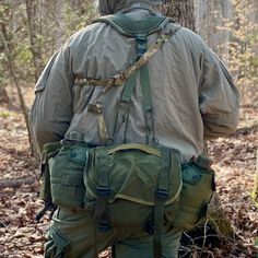 a man in the woods with his back to the camera, wearing an army uniform