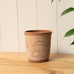 a clay pot sitting on top of a wooden table next to a green leafy plant