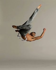 a man flying through the air while riding on top of a skateboard in front of a gray background