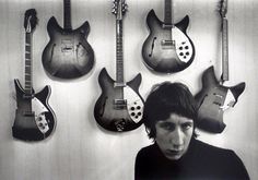 black and white photograph of a man in front of guitars hanging on the wall behind him