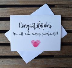 congratulations card with pink heart on white envelope sitting on wooden table next to pen and paper