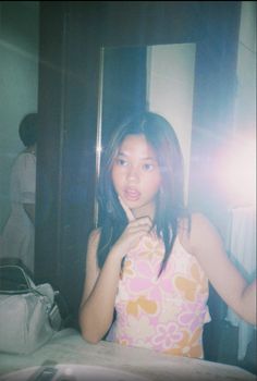 a woman standing in front of a mirror with her hand on her chin and looking at the camera