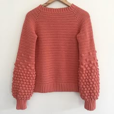 an orange sweater hanging on a hanger with a white wall in the back ground