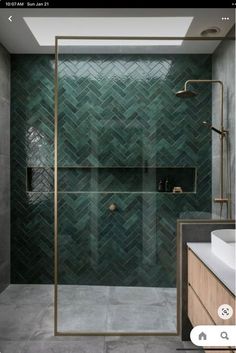 a green tiled bathroom with a shower and sink in the corner, next to a large mirror