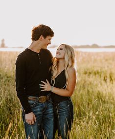 a young man and woman standing in tall grass looking into each other's eyes