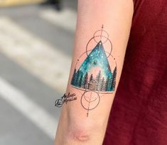 a person with a tattoo on their arm has a triangle and trees in the background