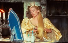 a woman in a golden dress sitting at a table with a blue mirror and candle