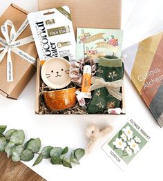 an assortment of items in a box on top of a white table with greenery